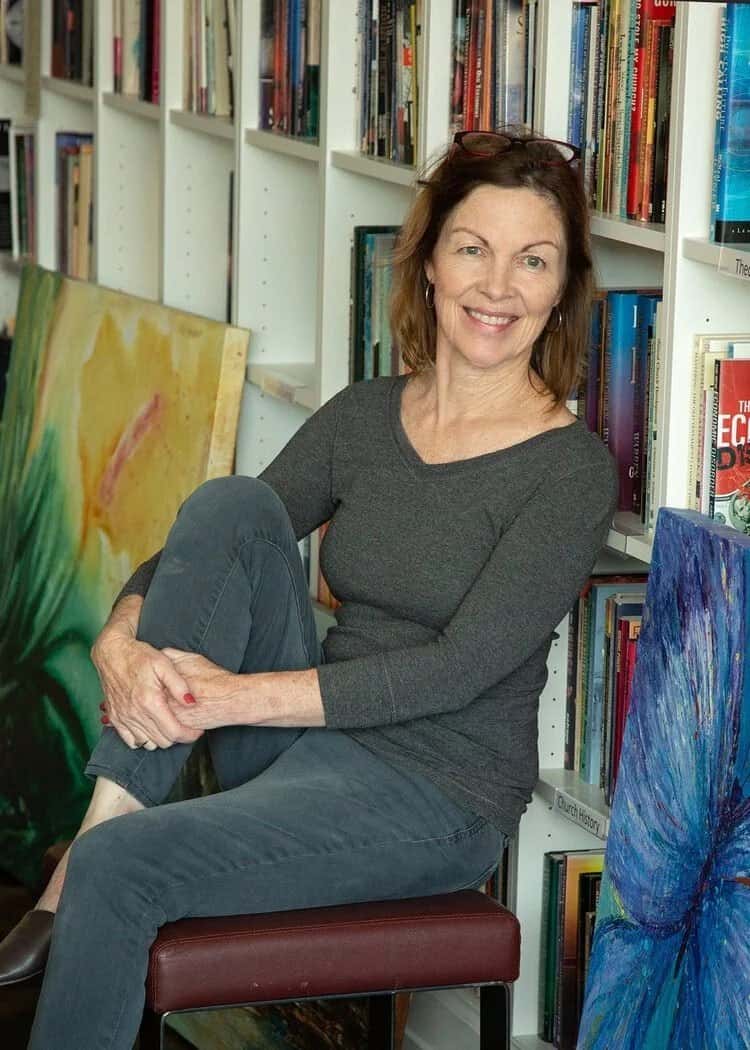 Barbie Hunt seated in her studio, smiling, with bookshelves and paintings behind her
